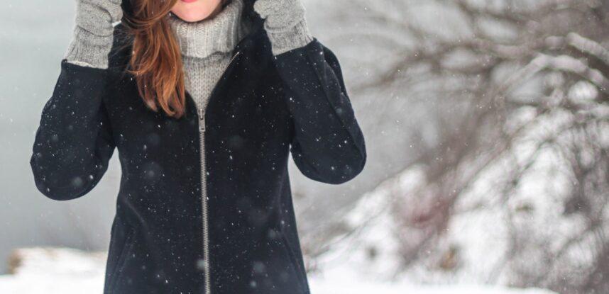 A woman enjoying a snowy winter day, dressed warmly and smiling.